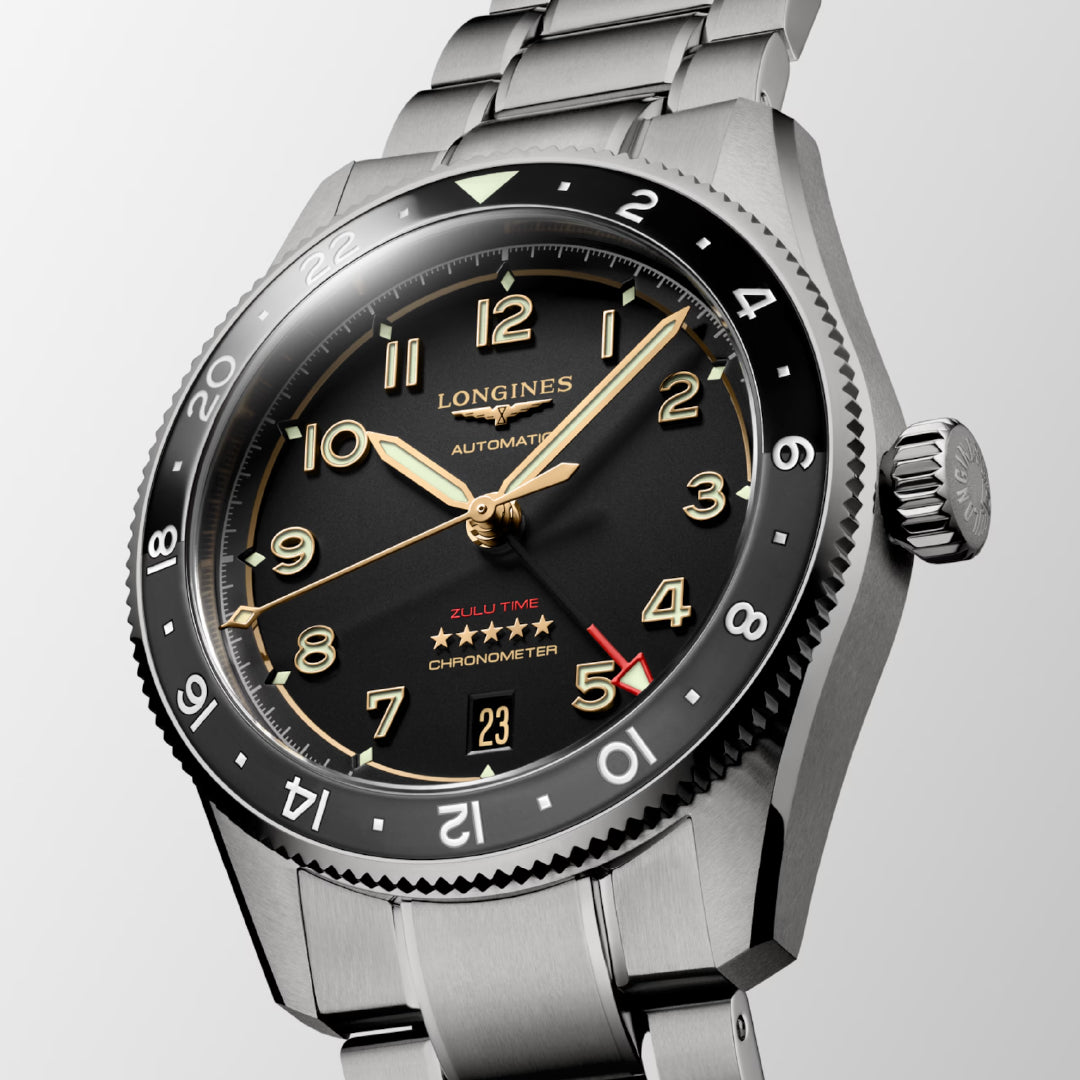 A close-up of the Longines Spirit Zulu Time Titanium Case and Titanium Automatic 39mm Watch reveals its black dial featuring gold hour markers and a red arrow on the 24-hour bezel. The watch proudly displays "Zulu Time" and "Chronometer-certified" above small stars, with the date window showing the number 23.