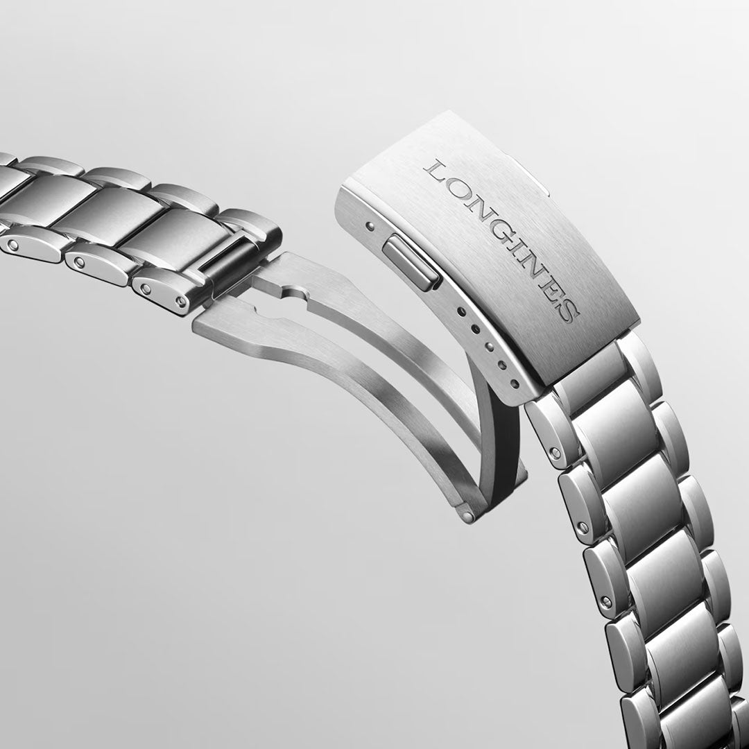 A close-up of a stainless steel bracelet from the Longines Spirit Zulu Time Automatic 39mm Watch, featuring a partially open clasp engraved with the Longines brand name. Set against a plain light gray background, the image highlights the refined craftsmanship of this dual time zone watch.