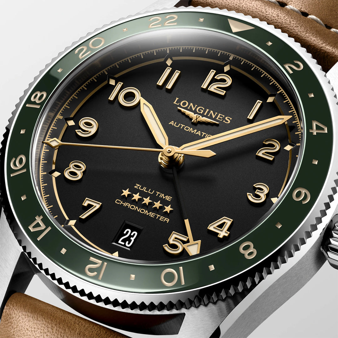 The Longines Spirit Zulu Time Automatic 39mm Watch has a black dial with gold Arabic numerals and hands, a dark green bezel with ceramic insert, and a brown leather strap. It features "Automatic" and "Zulu Time" on the dial and a date window at 6 o'clock.