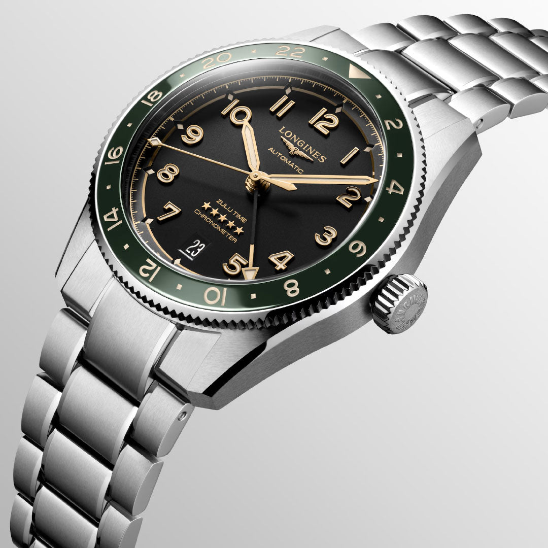 A close-up of the Longines Spirit Zulu Time Automatic 39mm Watch, a chronometer-certified dual time zone watch with a black and green dial, silver markers, gold hands, date at 6 o’clock, and a polished stainless steel bracelet.