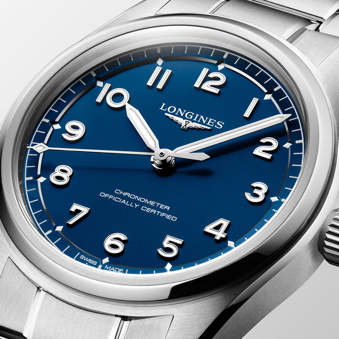 A close-up of the Longines Spirit Pilot Automatic 39mm Watch by Longines, featuring a silver case, blue dial with white Arabic numerals, and silver hands set to 10:10. The dial displays the inscription “CHRONOMETER OFFICIALLY CERTIFIED,” underscoring its chronometer certification.