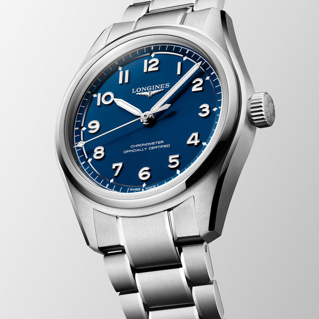 A Longines Spirit Pilot Automatic 39mm Watch in silver, featuring a striking blue dial with white Arabic numerals and a stainless steel bracelet, is displayed at an angle against a light background. This distinguished timepiece from Longines seamlessly blends classic aviator style with chronometer-certified precision and reliability.