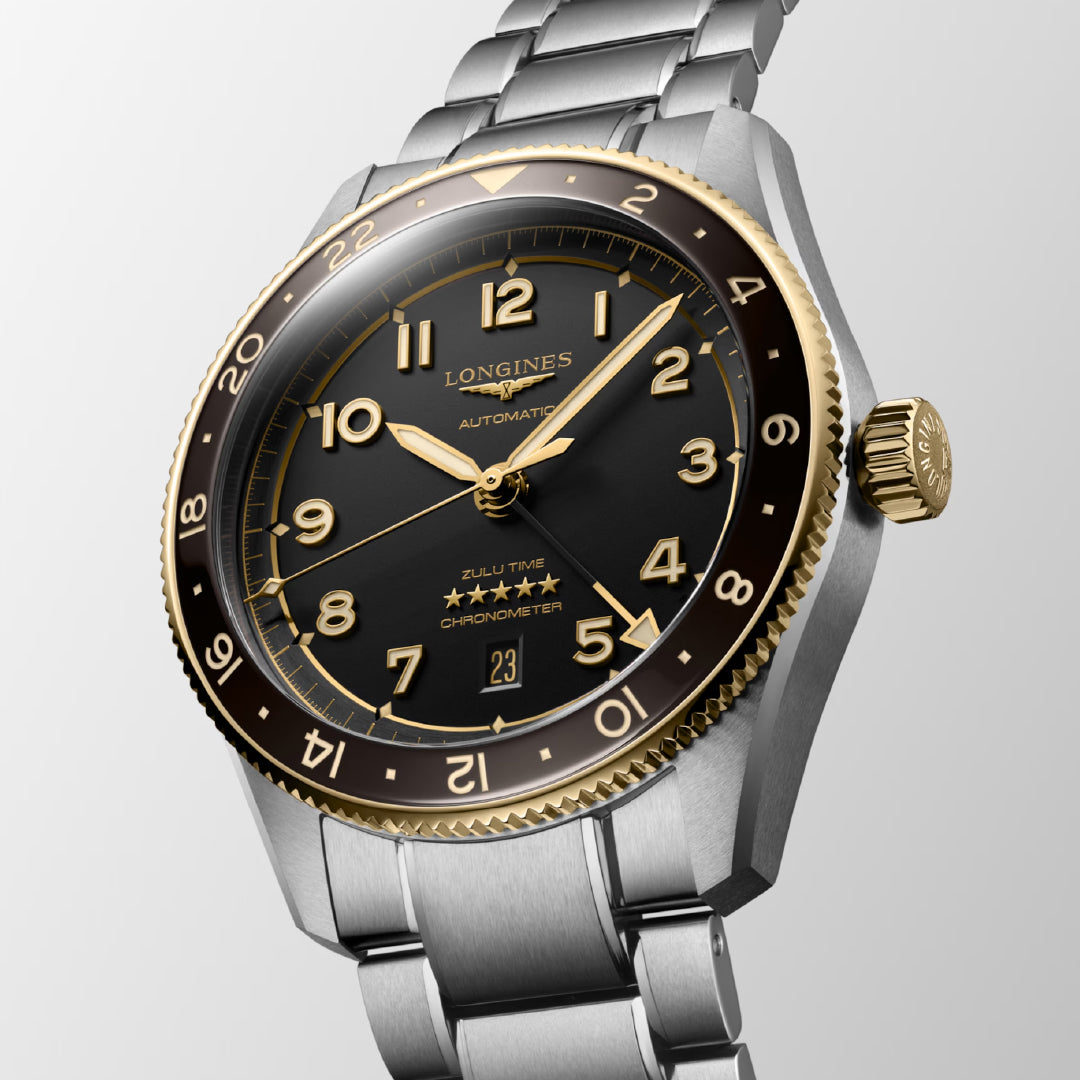 The Longines Spirit Zulu Time Automatic 42mm Watch exudes luxury with its silver and gold design showcasing a black dial, gold numerals, dual time zones, and date display. Its elegant metal bracelet perfectly complements the striking gold bezel of this chronometer-certified masterpiece.