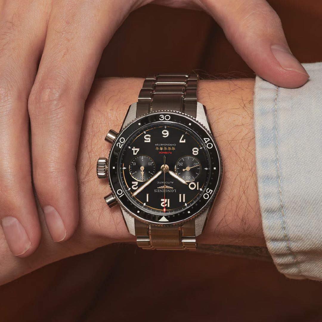 Close-up of a man's wrist adorned with the Longines Spirit Flyback Titanium Automatic 42mm watch. Evoking classic aviators' style, this elegant and precise timepiece features a black dial with three subdials and a rotating bezel, while another hand gently grips the wrist.