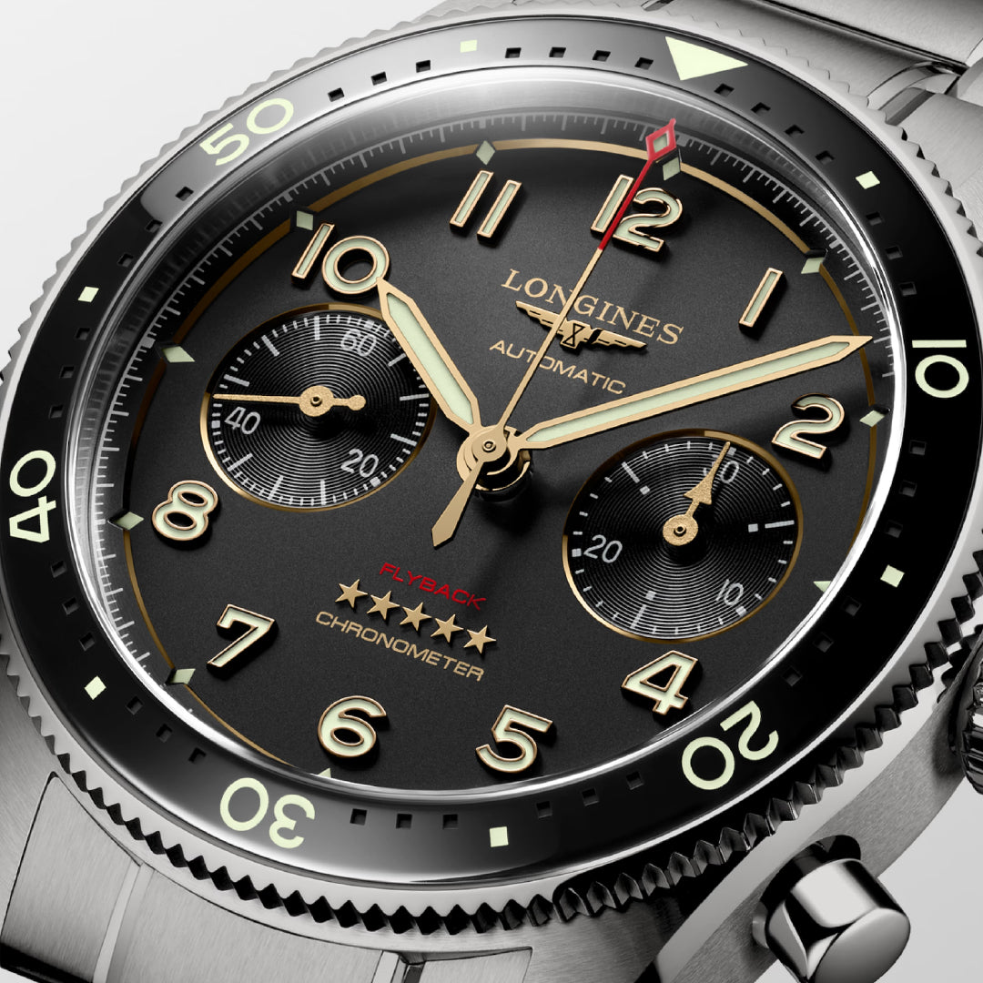 Close-up of a Longines Spirit Flyback Titanium Automatic 42mm Watch, celebrated among aviators' watches, showcasing a black dial with gold and white hour markers, three subdials, gold hands, an engraved bezel with numbers, and a striking red-tipped second hand.