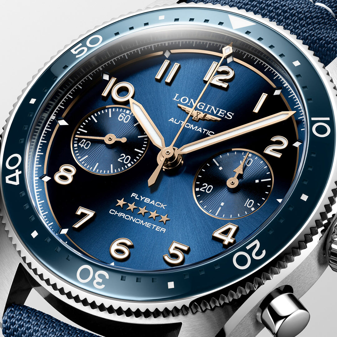 The Longines Spirit Flyback Automatic 42mm Watch features a blue dial and bezel, silver-toned hands and numerals, two sub-dials, and a blue fabric strap. The aviator's timepiece includes minute indicators on its bezel.