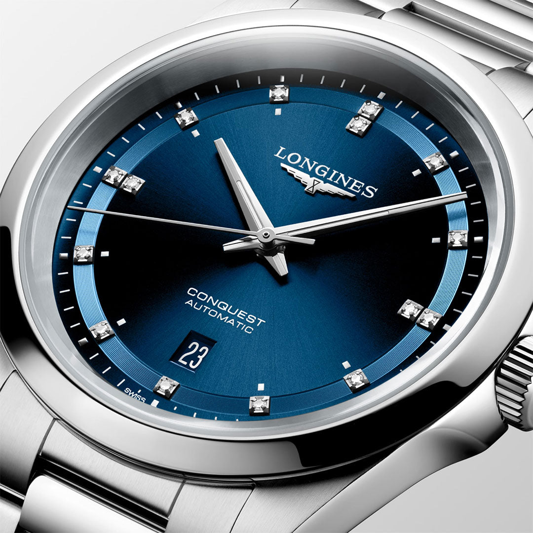 A close-up of the Longines Conquest Automatic 41mm watch by Longines, featuring a striking blue dial, silver-toned hands, diamond hour markers, a date window at 6 o’clock, and a refined stainless steel case and bracelet—an elegant Swiss timepiece crafted to enhance your everyday style.