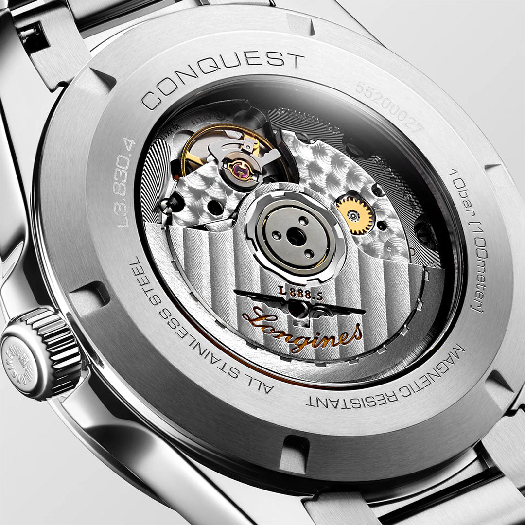 Close-up of the back of the Longines Conquest Automatic 41mm Watch, revealing its intricate automatic movement with visible gears and the “Longines” engraving on the rotor. The stainless steel case features technical specifications, showcasing the robust craftsmanship that makes this Swiss-made timepiece an excellent choice for everyday wear.