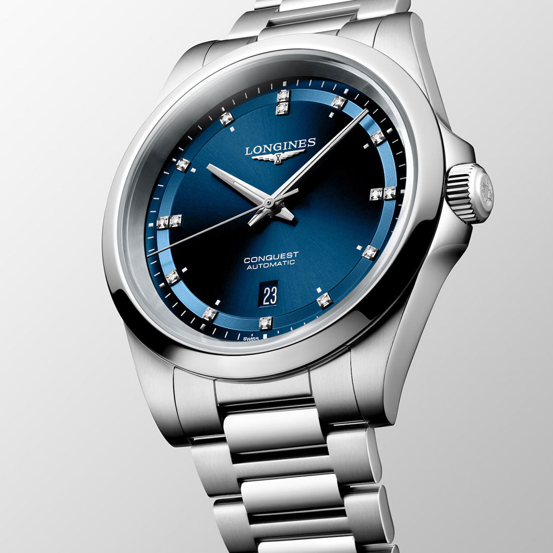 The Longines Conquest Automatic 41mm Watch features a sleek silver case with a metallic band, a striking blue dial set with diamond hour markers, and a date display at 6 o’clock. The face proudly displays “Longines Conquest Automatic,” making this timepiece by Longines an elegant yet practical choice for everyday sophistication.