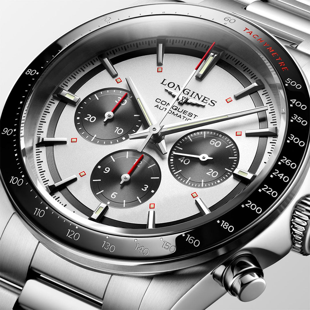 Close-up of a Longines Conquest Chronograph Automatic 42mm watch with a silver dial, three subdials, black bezel, red accents, and stainless steel bracelet. The time shown is 10:08:37.