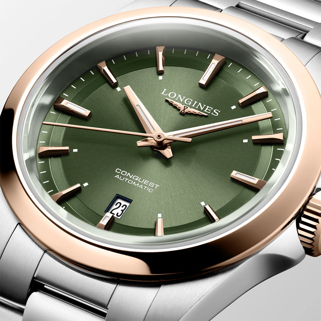 A close-up of the Longines Conquest Automatic 30mm Watch by Longines, featuring a green dial, rose gold bezel, silver hour markers, date window at 6 o'clock, and a two-tone stainless steel bracelet.