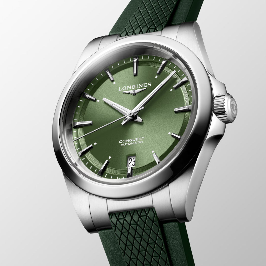 The Longines Conquest Automatic 38mm Watch features a green dial, silver hands and indices, date at 6 o’clock, stainless steel case, and green textured strap—an everyday timepiece displayed on a light gray background.