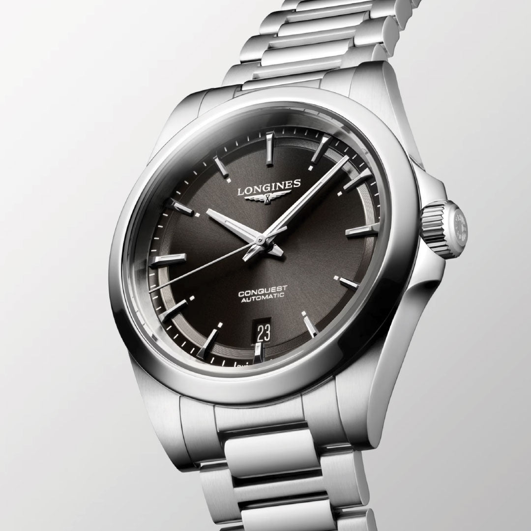 The Longines Conquest Automatic 38mm Watch features a silver stainless steel bracelet, black dial, silver hour markers, and a date at 6 o'clock—an ideal everyday watch from Longines, shown angled on a light background.