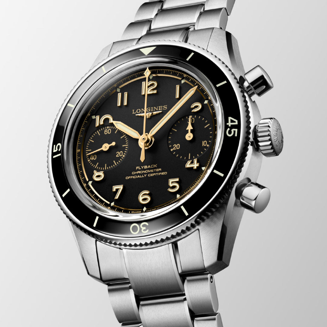 The Longines Spirit Pilot Flyback Automatic Manual Winding 39.5mm watch is shown angled on a light gray background, highlighting its black dial, gold-tone Arabic numerals, two subdials, and flyback chronograph features.
