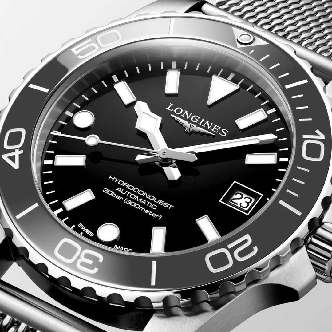 Close-up of the Longines Hydroconquest Automatic 39mm watch with a black dial, white hour markers, date at 3 o’clock, and stainless steel mesh bracelet. Features a water-resistant (300m) bezel with minute markings.