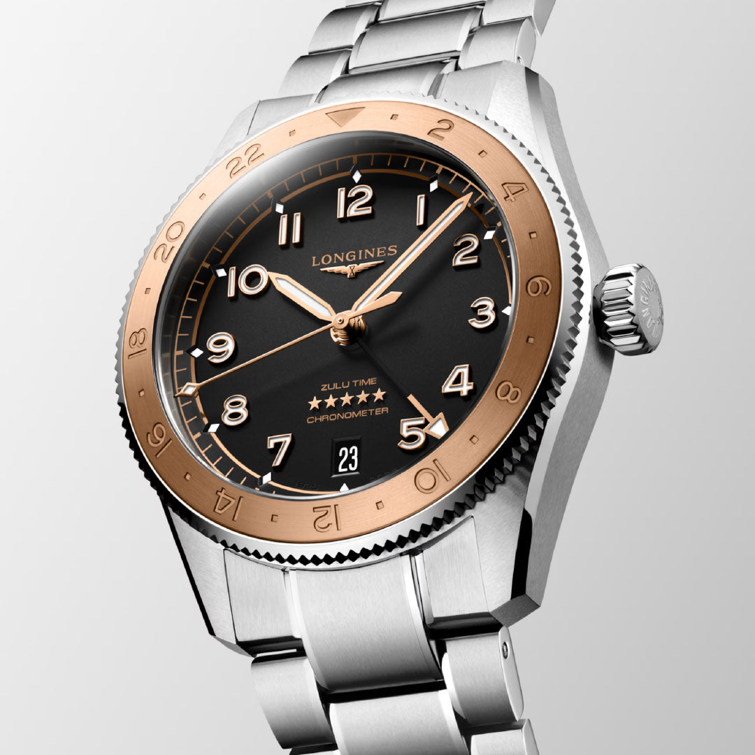 A close-up of the Longines Spirit Zulu Time 1925 Automatic 39mm Watch features a stainless steel bracelet, black dial, rose gold bezel with numerals, gold-tone hands, date at 6 o’clock, and dual time zones.