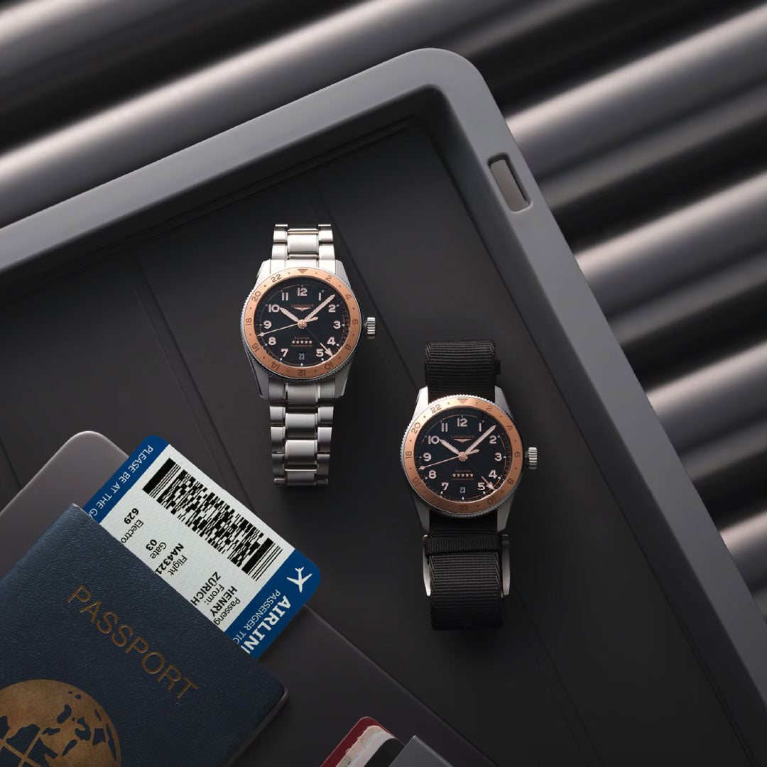 A Longines Spirit Zulu Time 1925 Automatic 39mm Watch with a metal band and another watch with a black fabric strap rest in a security tray with a passport, boarding pass, and credit cards at an airport checkpoint.