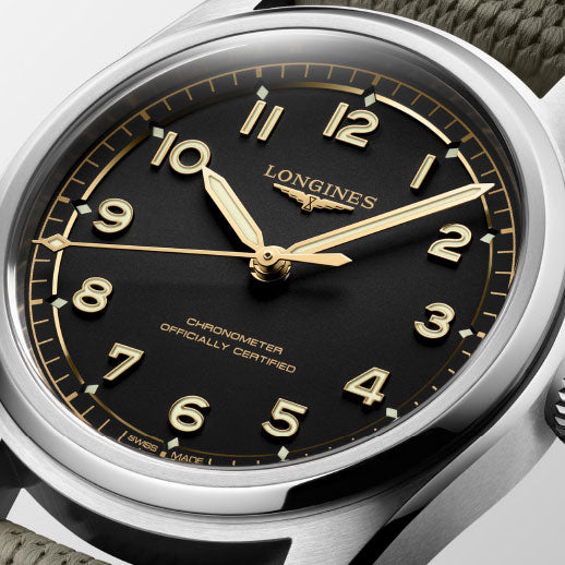 A close-up of the Longines Spirit Pilot Automatic 39mm watch featuring a black dial, gold numerals and hands, "Longines" and "Chronometer Officially Certified" on the face, and a textured green strap.