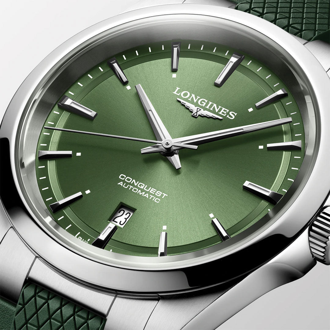 A close-up of the Longines Conquest Automatic 41mm Watch features a green dial, silver hour markers, date window at 6 o’clock, stainless steel case, and textured green strap—highlighting Longines’ sporty elegance.