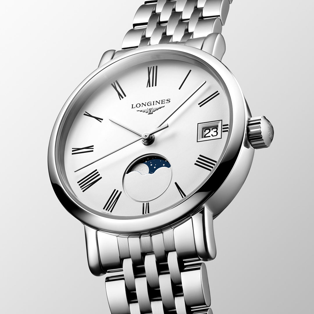 A close-up of the Longines Elegant Collection Moonphase Quartz 30mm Watch reveals a silver wristwatch featuring a white dial with Roman numerals, a date window showing "23," and a moon phase indicator. This watch from Longines exudes minimalist elegance with its polished metal link bracelet and timeless design.