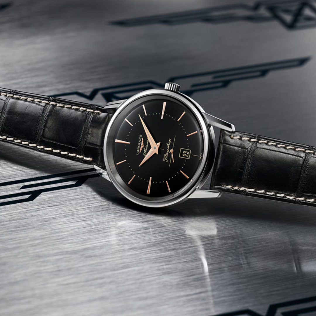The Longines Flagship Heritage Automatic 38.5mm Watch exudes timeless elegance with its black leather strap, black dial, silver case, gold hour markers, and date display—reflecting the classic style of Longines.