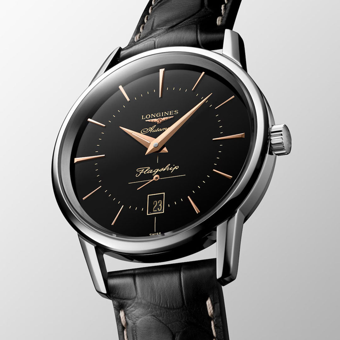 A close-up of the Longines Flagship Heritage Automatic 38.5mm watch, featuring a black dial, gold hour markers, enamel caravel medallion on the caseback, date at 6 o’clock, and a black leather strap—an ideal classic from Longines.