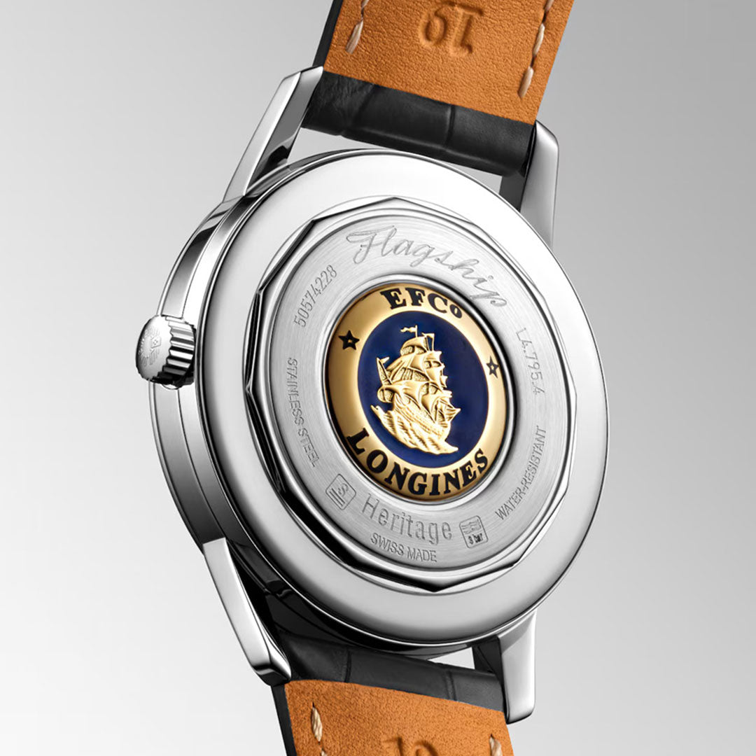 A close-up of the Longines Flagship Heritage Automatic 38.5mm Watch reveals a "Flagship" engraving and caravel medallion on a blue back, encircled by "EFCO LONGINES", with its leather strap emphasizing classic Longines style.