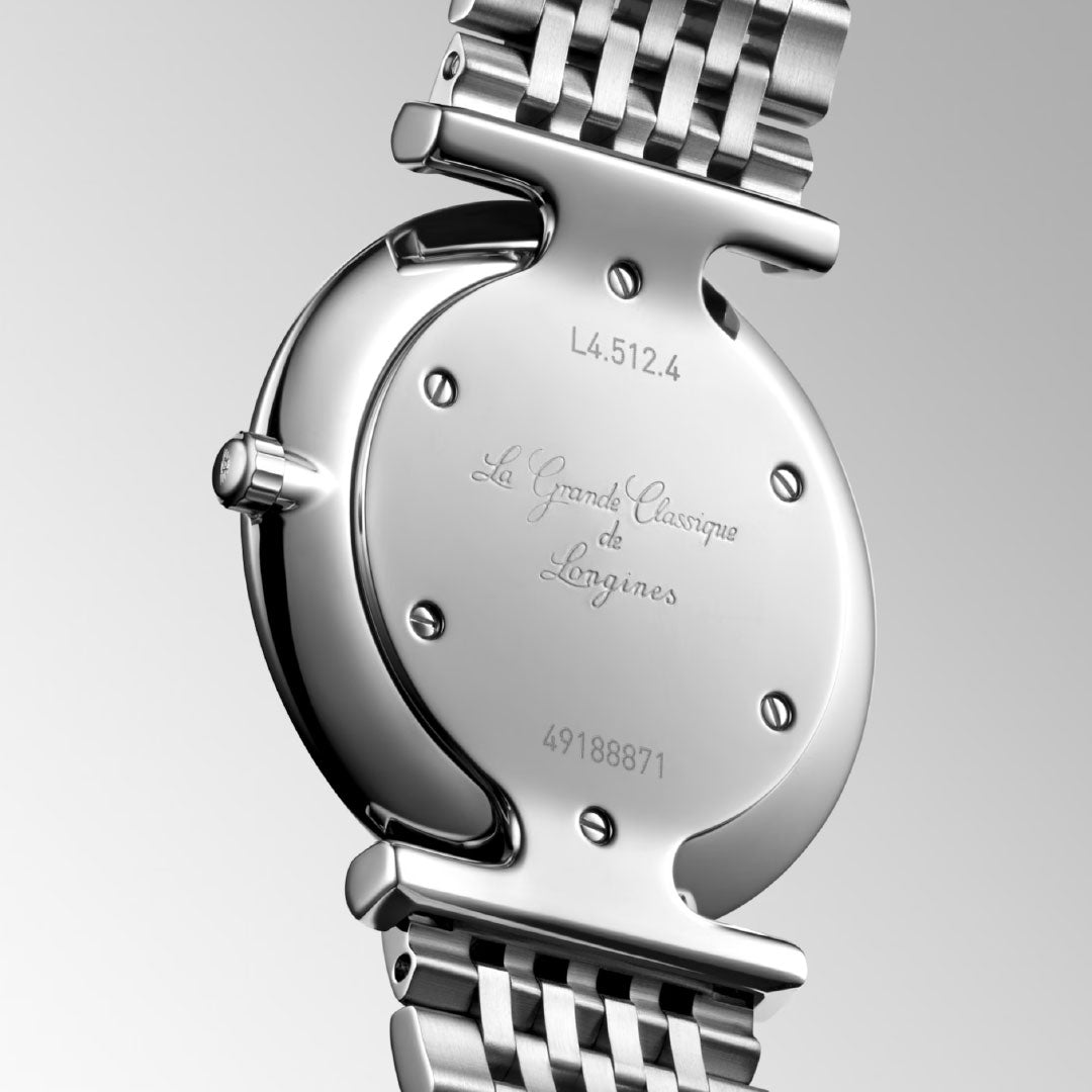 Close-up of the back of a Longines La Grande Classique Quartz 29mm watch, showing engraved inscription and serial numbers on its silver case and metal link bracelet, set against a light gray background.