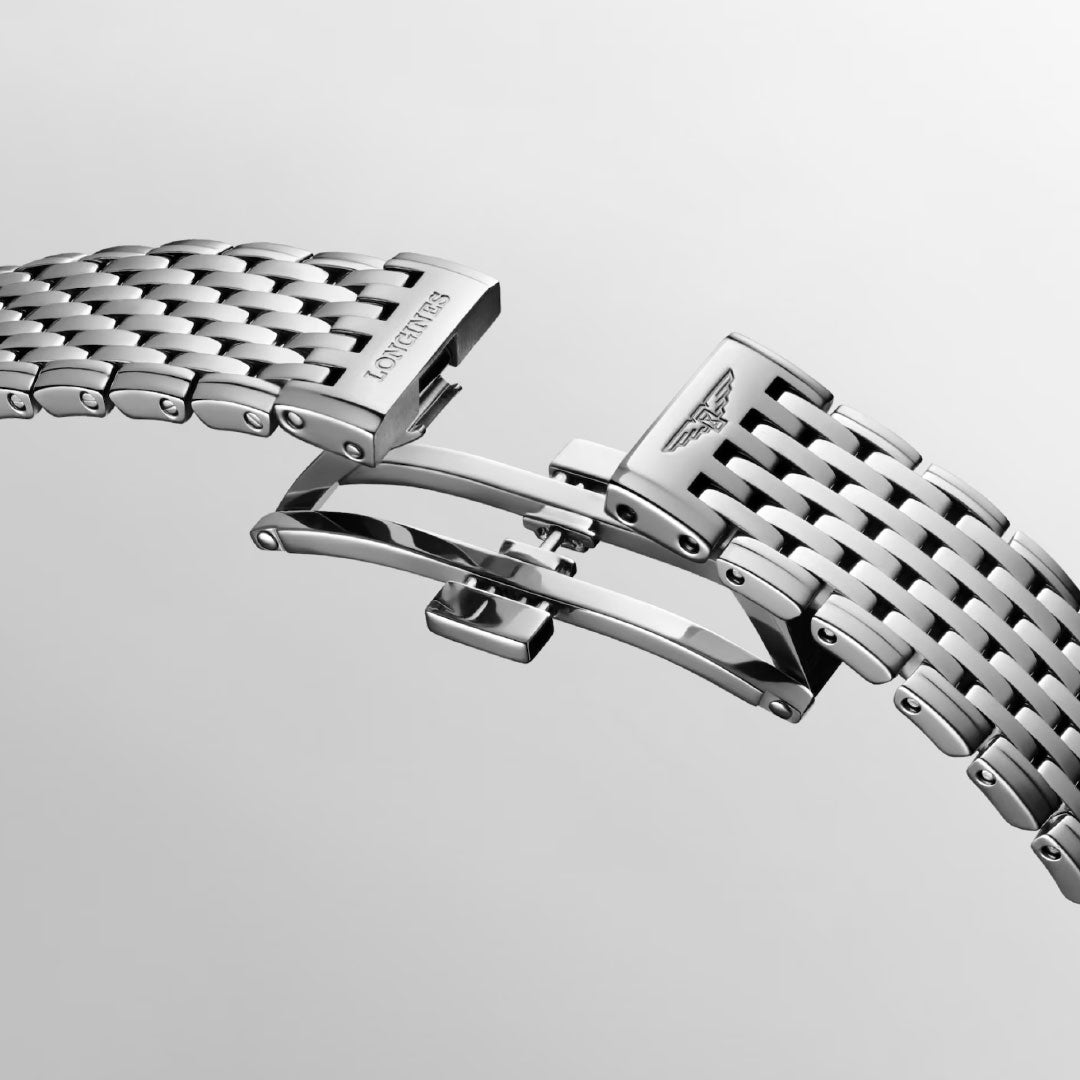 A close-up of the stainless steel Longines La Grande Classique Quartz 29mm bracelet with an open butterfly clasp, featuring the engraved Longines logo and woven links—an elegant detail against a light grey background.