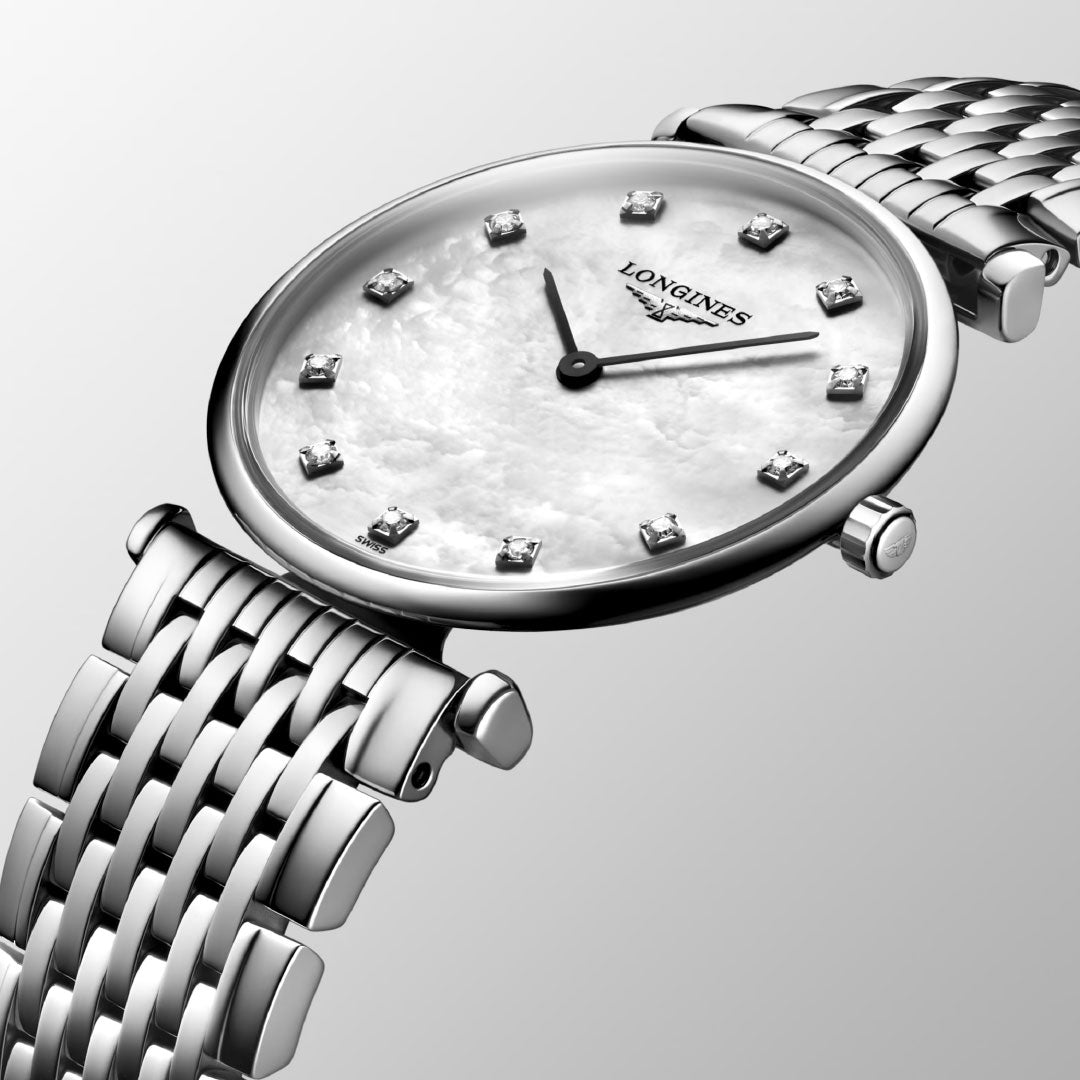 The Longines La Grande Classique Quartz 29mm Watch features a silver case, white mother-of-pearl dial with diamond hour markers, and a metal link bracelet, exemplifying classic elegance against a light gray background.