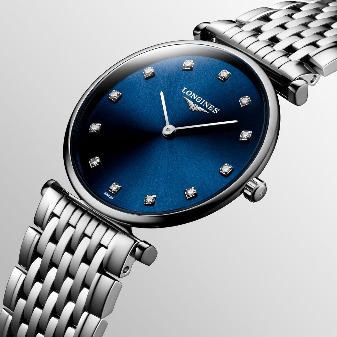 A close-up of the Longines La Grande Classique Quartz 29mm Watch features a blue sunburst dial with diamond markers, silver hands, and a polished silver link bracelet, displayed against a light gray background for an elegant look.
