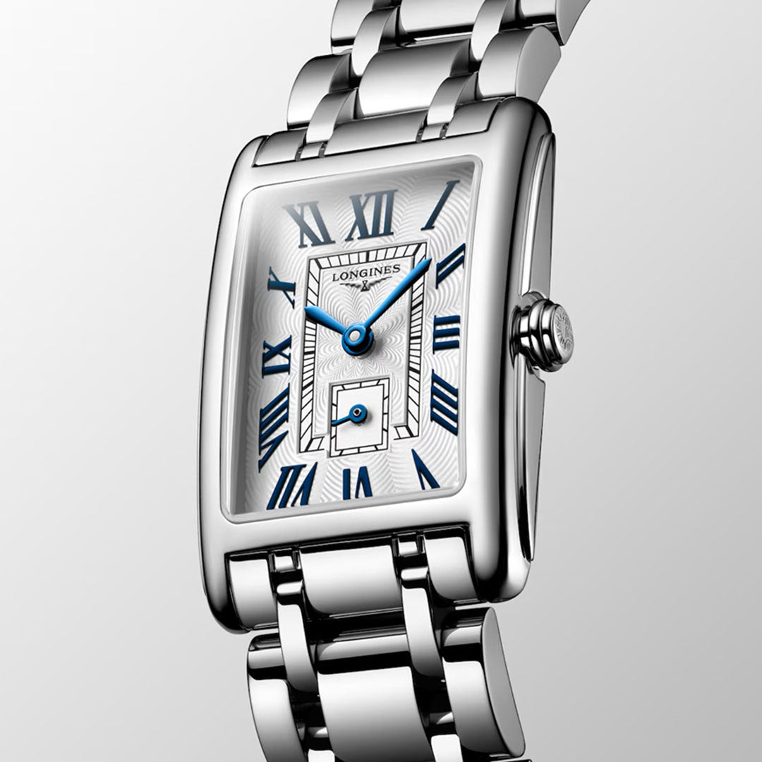 The Longines Dolcevita Quartz 20.8 x 32mm Watch features a silver rectangular case, white dial with blue Roman numerals, and a metal link bracelet—exuding timeless elegance and luxury against a subtle gradient backdrop.