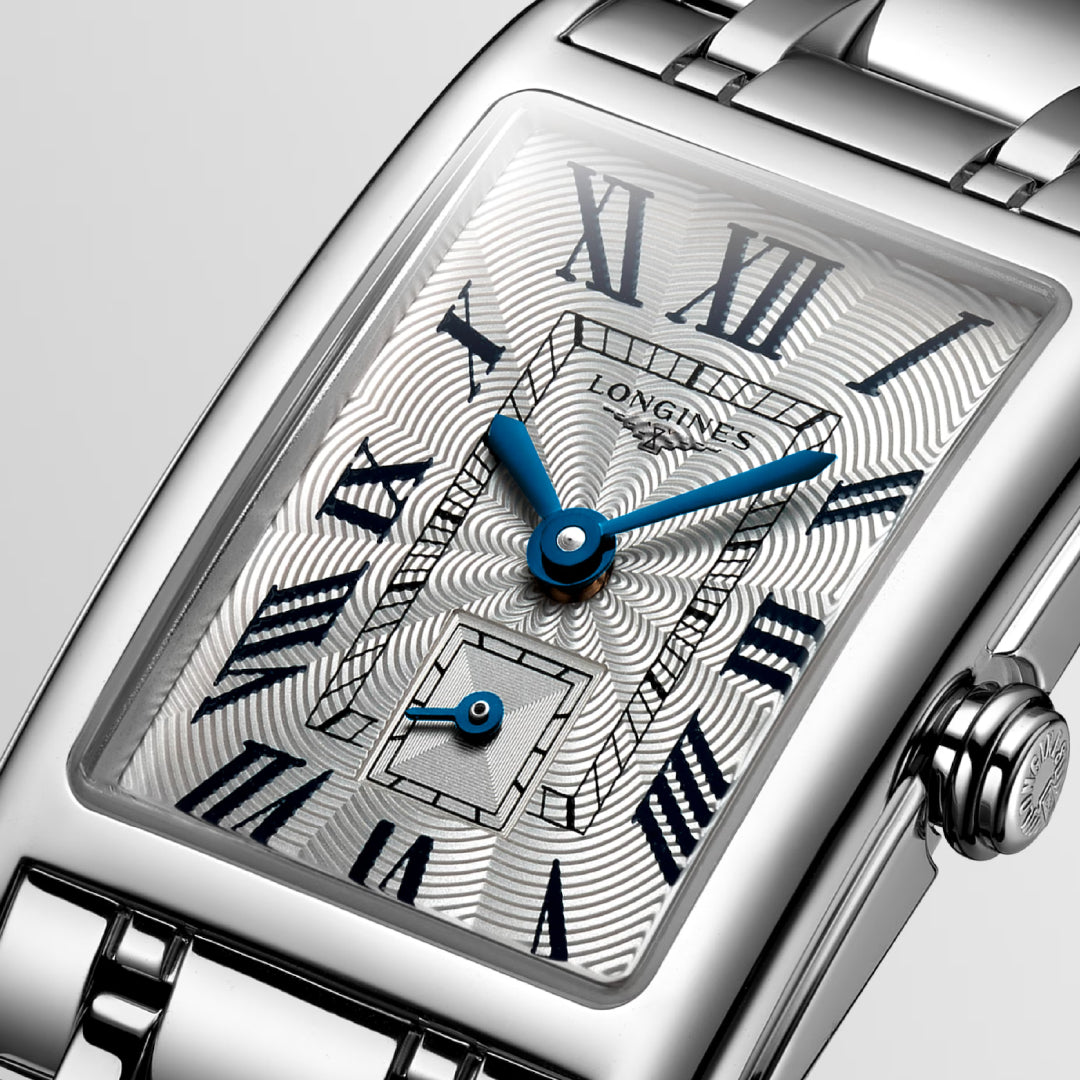 A close-up of the Longines DolceVita Quartz 20.80 X 32mm Watch reveals a rectangular silver design with a textured dial and blue Roman numerals. The Longines brand name is prominent, capturing its spirit. A metal link band enhances its elegance, complemented by a smaller subdial below.