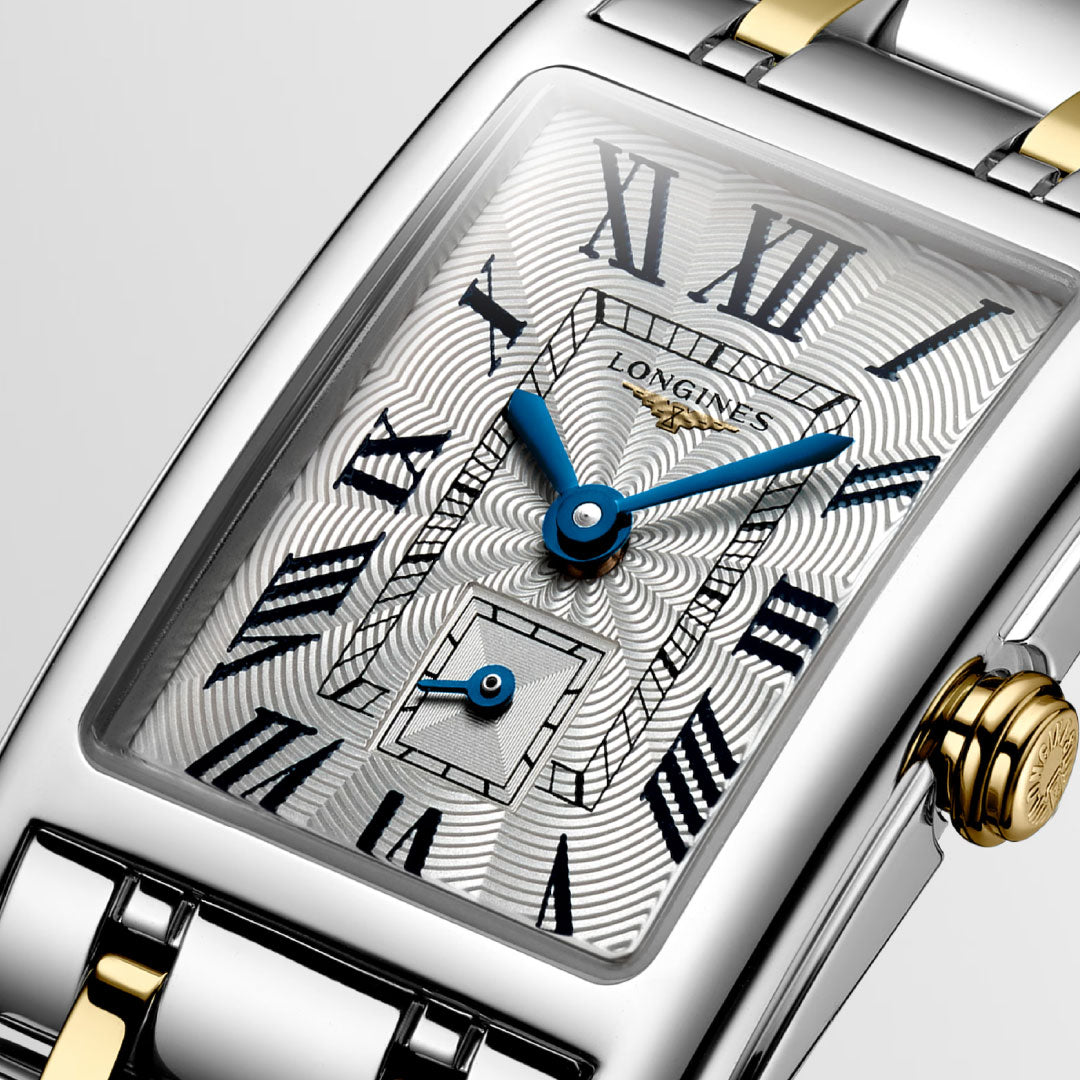 Close-up of the Longines Dolcevita Quartz 20.8 x 32mm Watch featuring a rectangular case, silver and gold metal band, blue hands, Roman numeral markers, patterned silver dial, and small seconds subdial at 6 o’clock.
