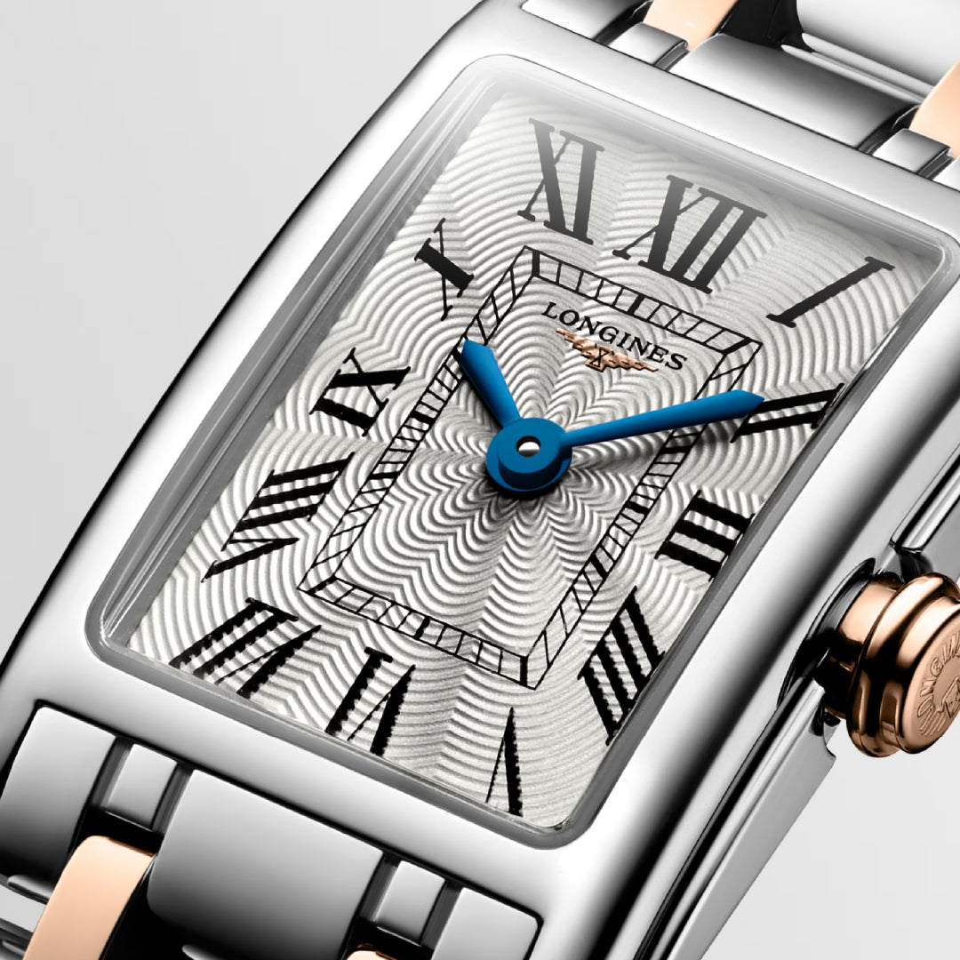 Close-up of a Longines Dolcevita Quartz 17.70 X 27mm watch, showcasing its rectangular face. This elegant piece features a silver and gold-tone band with a textured silver dial, blue hands, Roman numerals for hours, and an embossed crown with the iconic Longines logo.