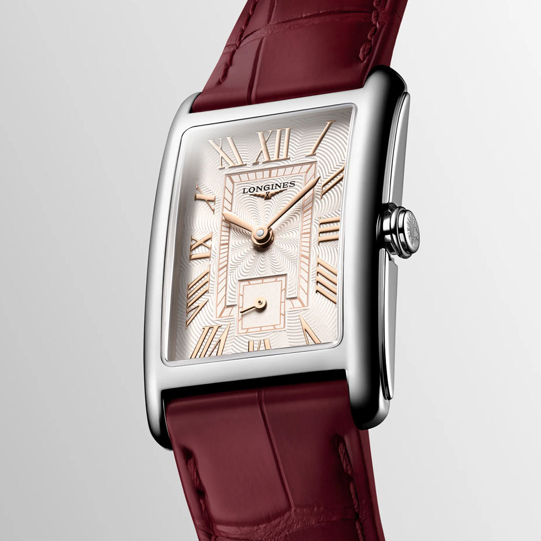 The Longines Dolcevita Quartz 23.3 x 37mm Watch features a silver rectangular case and a patterned white dial adorned with gold Roman numerals and a small seconds subdial. Complemented by a burgundy leather strap, this Longines timepiece embodies timeless elegance, beautifully presented against a light background.