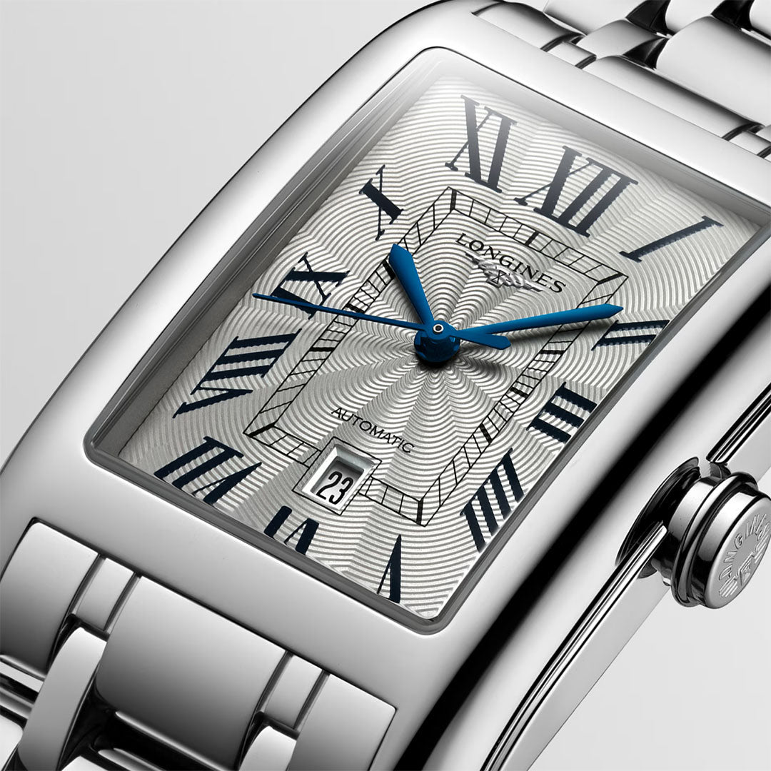 A close-up of the Longines Dolcevita Automatic 28.2 x 47mm Watch showcases its sleek silver rectangular case, blue hands, Roman numerals, and a sophisticated metal link bracelet. The date window displays “23,” while the intricately textured dial underscores Longines’s timeless elegance.