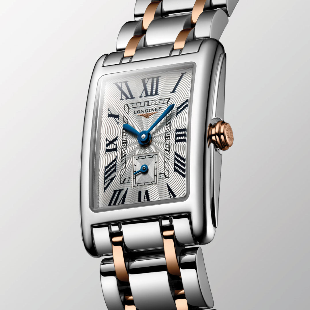 The Longines Dolcevita Quartz 20.8 x 32mm Watch boasts a silver and rose gold rectangular case, patterned silver dial, blue hands, Roman numerals, and date subdial—an elegant luxury piece by Longines.
