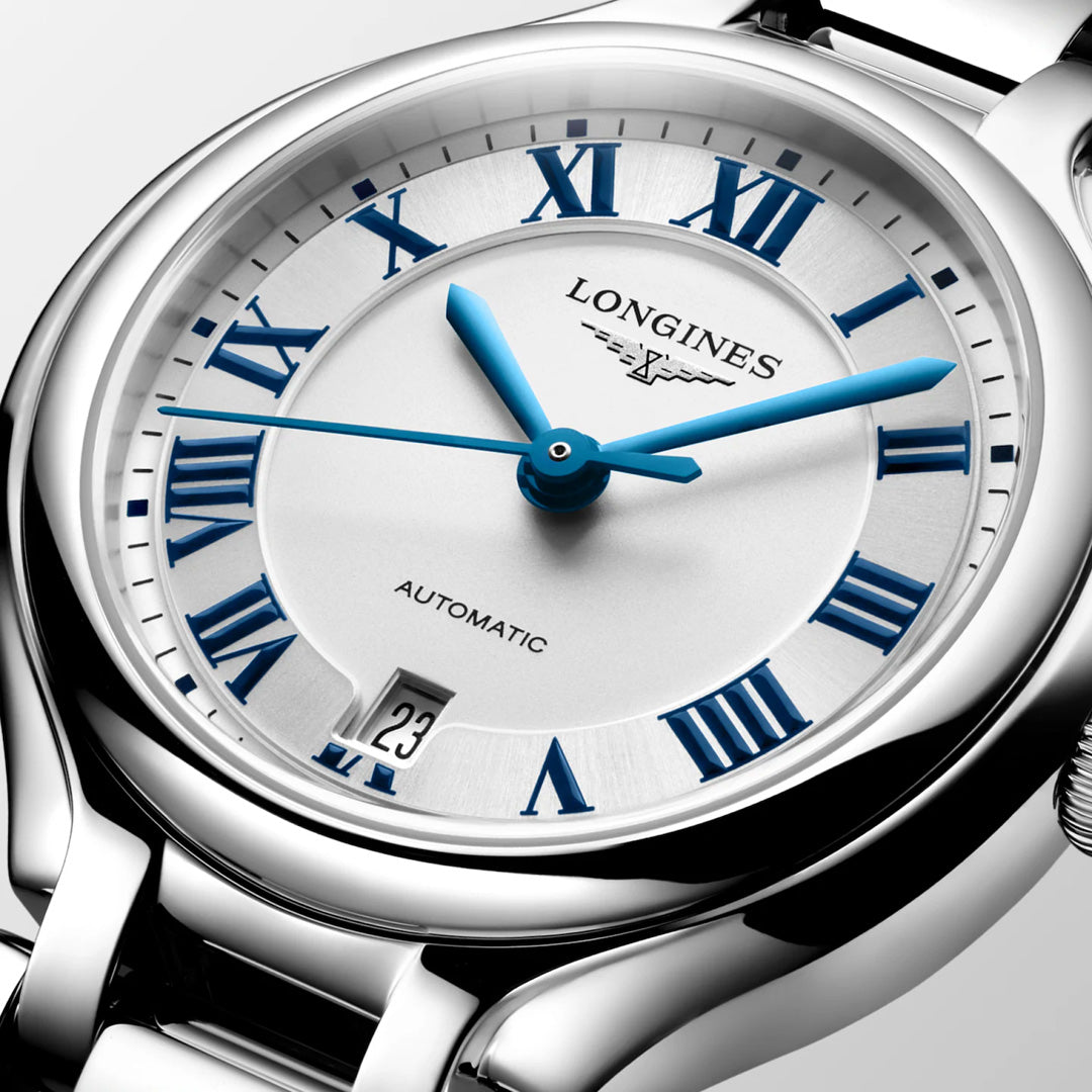 Close-up of the Longines PrimaLuna Automatic 30mm, a women’s luxury watch by Longines featuring a silver polished bracelet, white dial with blue Roman numerals and hands, and a date display at 3 o’clock.