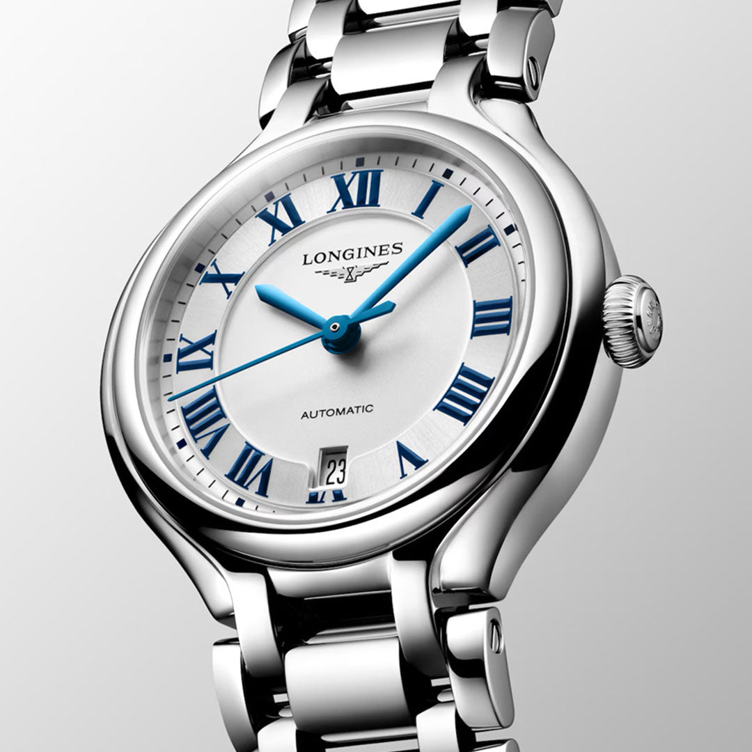 A close-up of the Longines Primaluna Automatic 30mm women's watch featuring a silver case, white dial with blue Roman numerals and hands, date window at 6 o'clock, and a polished metal bracelet.