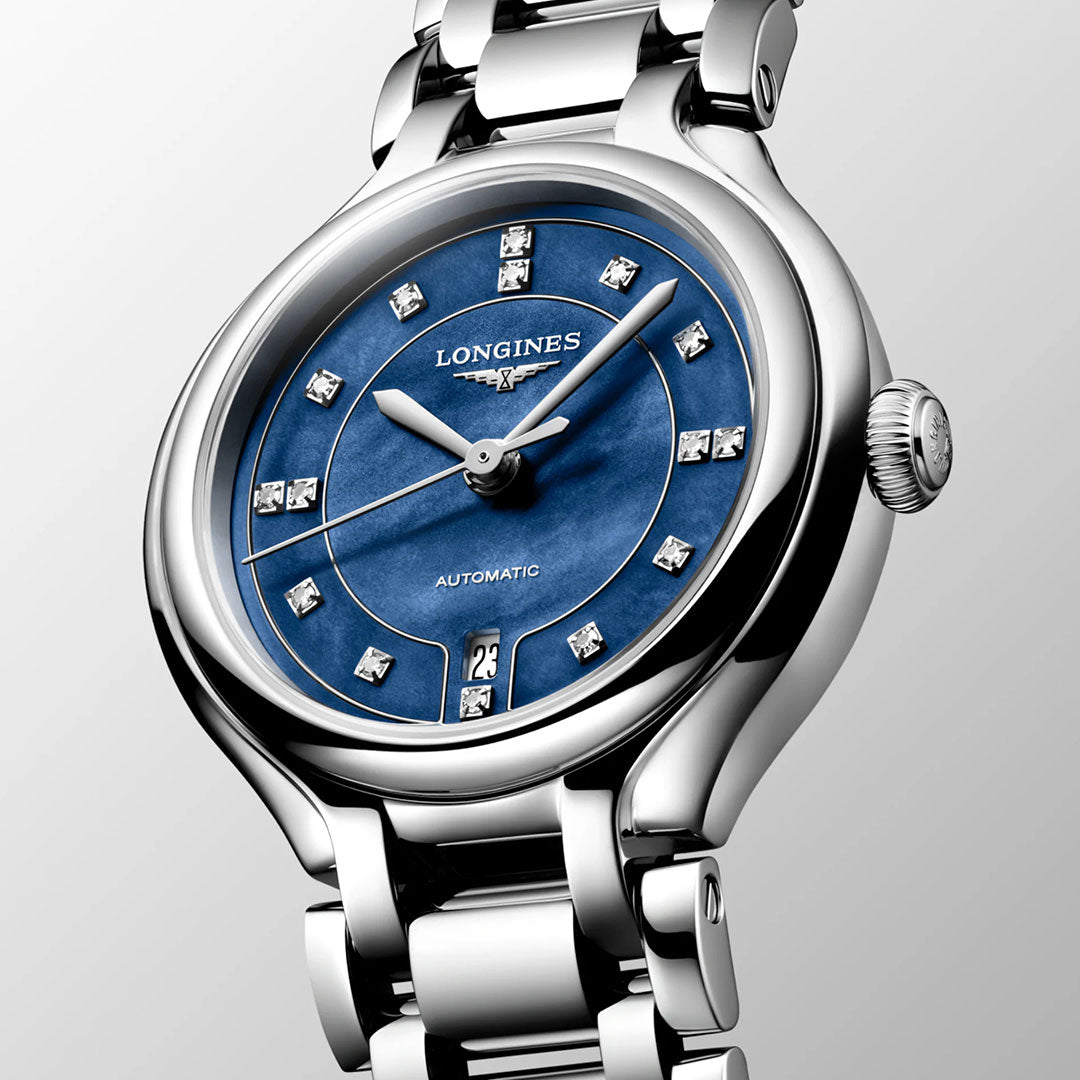 Introducing the Longines PrimaLuna Automatic 30mm Watch: a sophisticated women's timepiece by Longines, featuring a striking blue dial adorned with diamond hour markers, a date display at 6 o'clock, and a polished silver metal link bracelet. Photographed against a light gray background, this luxury watch is the ideal accessory for any occasion.