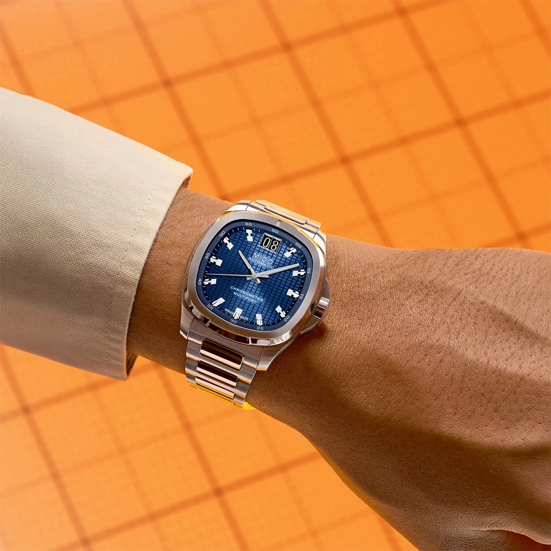 MIDO Multifort TV Big Date Chronometer Automatic 40mm Watch with a blue textured dial, silver-tone square case, and steel link bracelet, worn on a person’s wrist.