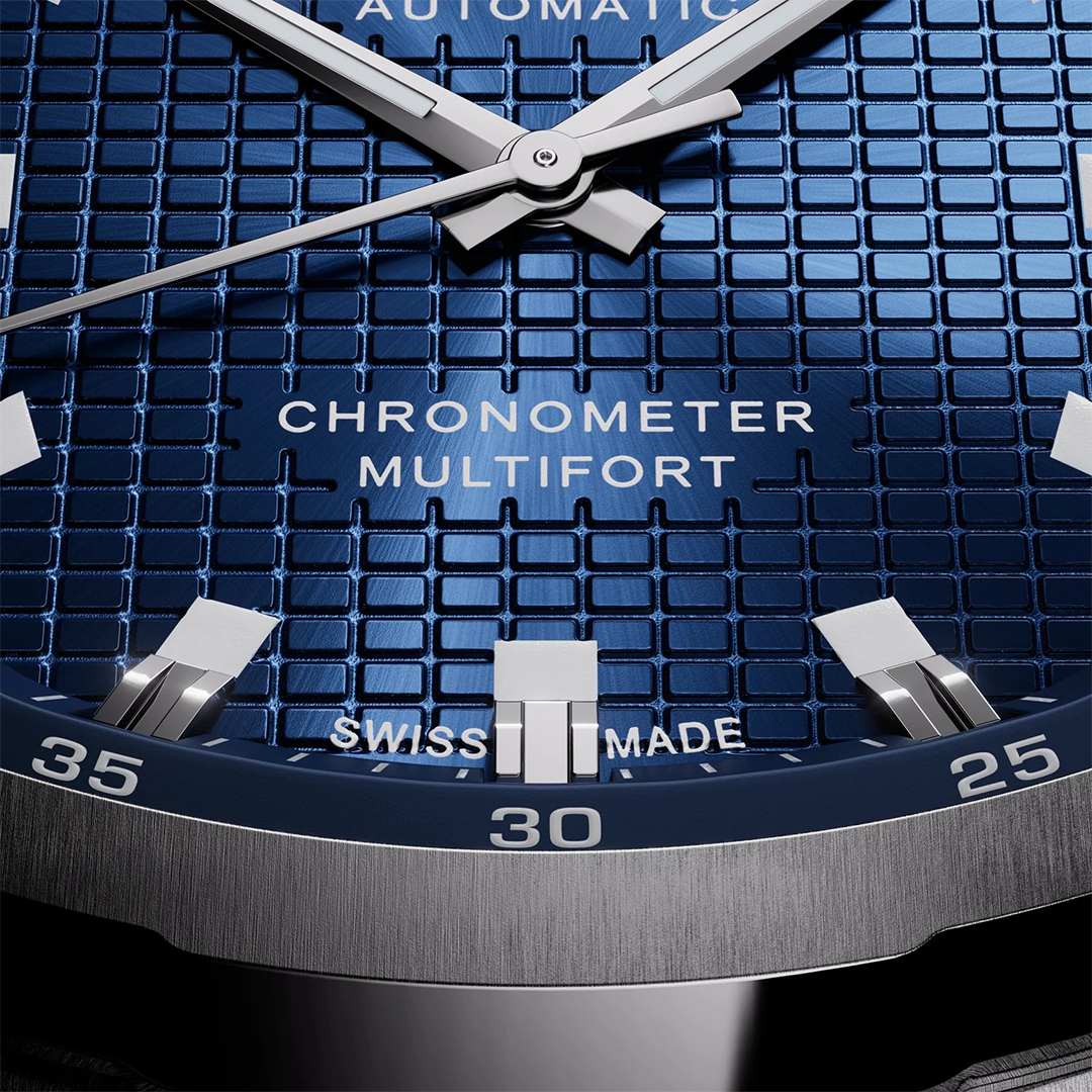 Close-up of a MIDO Multifort TV Big Date Chronometer Automatic 40mm Watch with a blue square-patterned dial, silver hands, hour markers, and the text “CHRONOMETER,” “MULTIFORT,” and “SWISS MADE.”