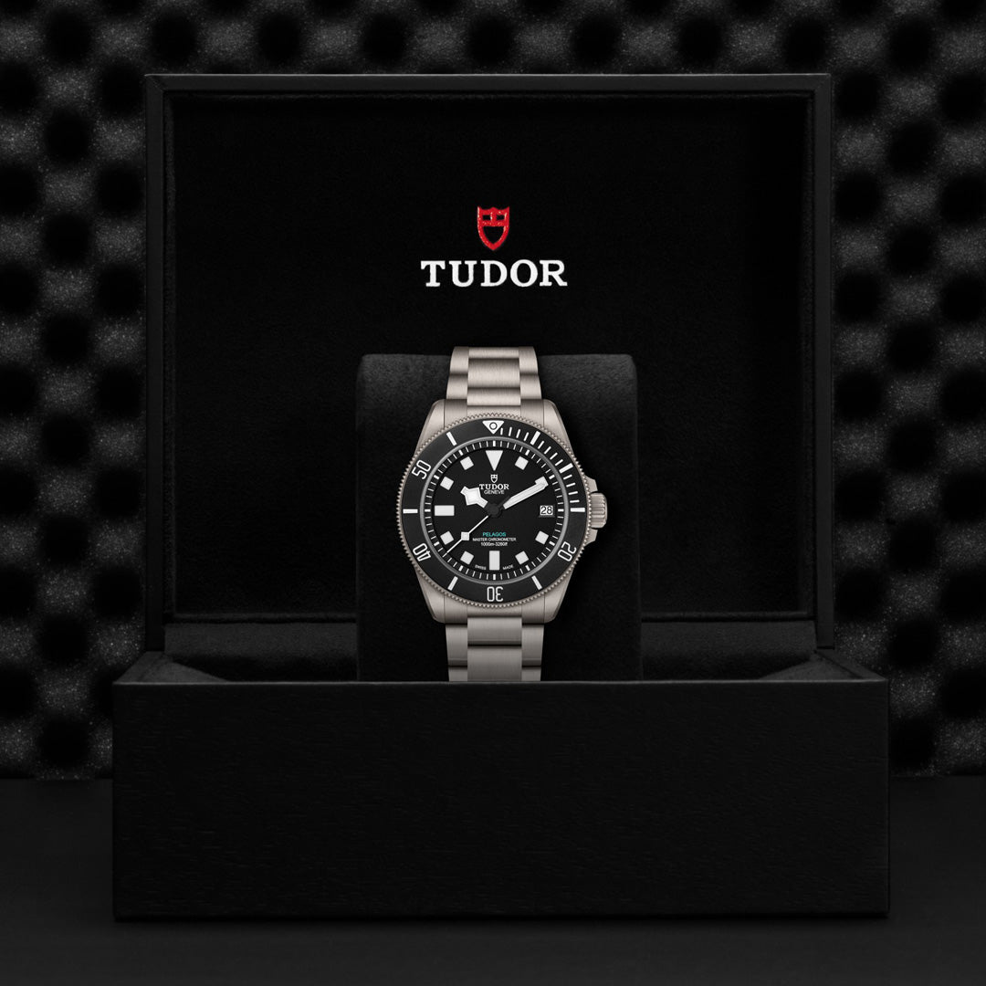 The TUDOR Pelagos Ultra watch with a black dial and silver bezel is showcased in an open black box. Featuring bold hour markers and a metal bracelet, this luxury timepiece exhibits Master Chronometer precision. The TUDOR logo is clearly visible on the inside lid of the box.