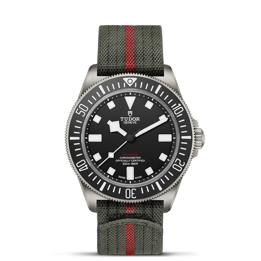 The TUDOR Pelagos FXD wristwatch is equipped with a stainless steel case and a black dial featuring prominent white hour markers. It includes a green fabric strap with a red stripe, designed for yacht racing enthusiasts. This water-resistant watch is a certified chronometer crafted for performance and adventure.