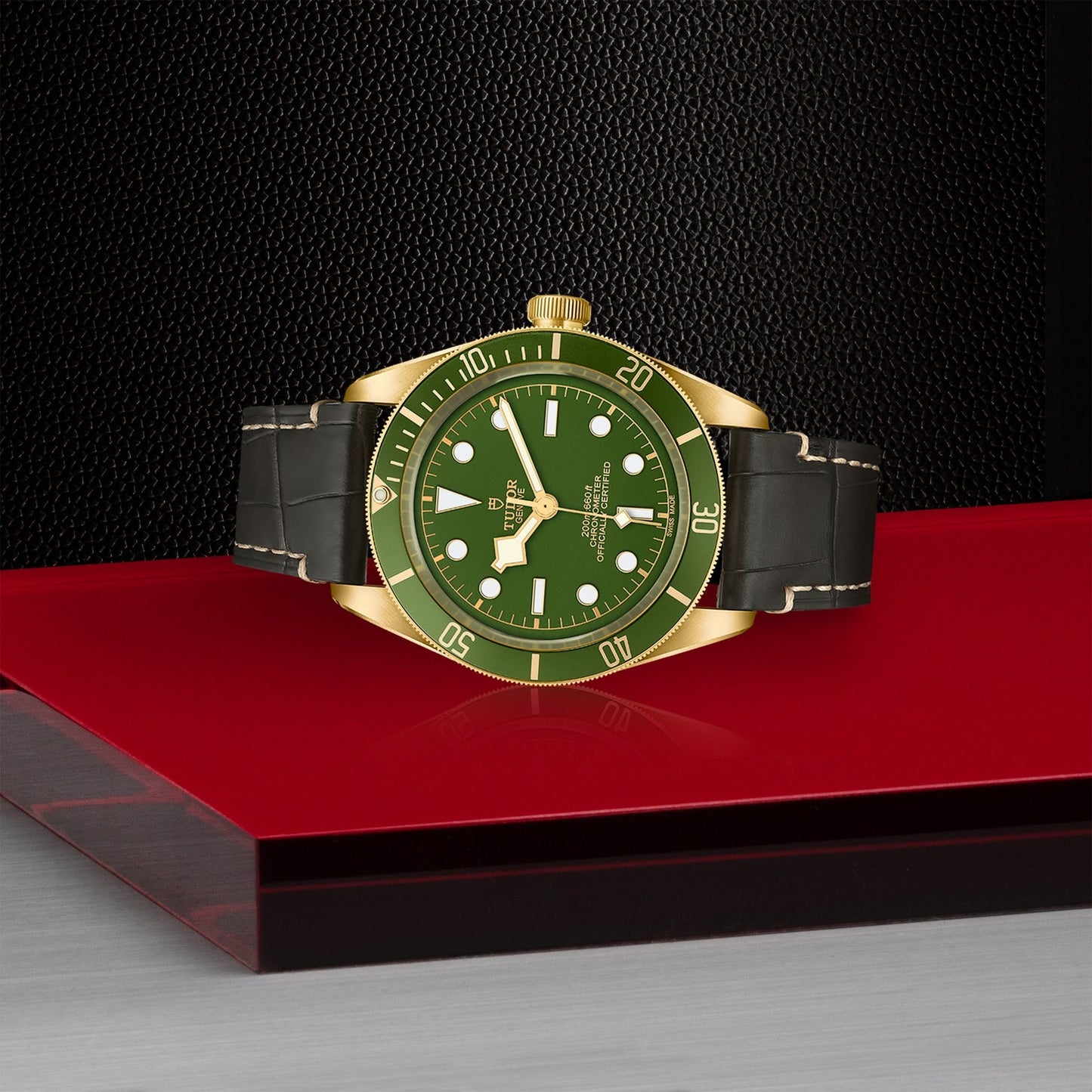 A luxurious timepiece from TUDOR, the Black Bay 58 18K wristwatch features a green face and bezel, complemented by gold accents and a leather strap. It evokes the classic Black Bay 58 design while resting elegantly on a red and black platform that combines timeless charm with modern sophistication.