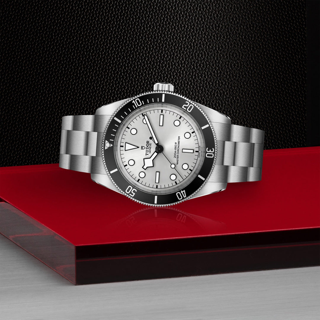 The TUDOR Black Bay 68 luxury wristwatch boasts a white dial, black bezel, snowflake hands, and luminous markers. A true Master Chronometer, it sits elegantly on a glossy red and black surface against a textured black background.