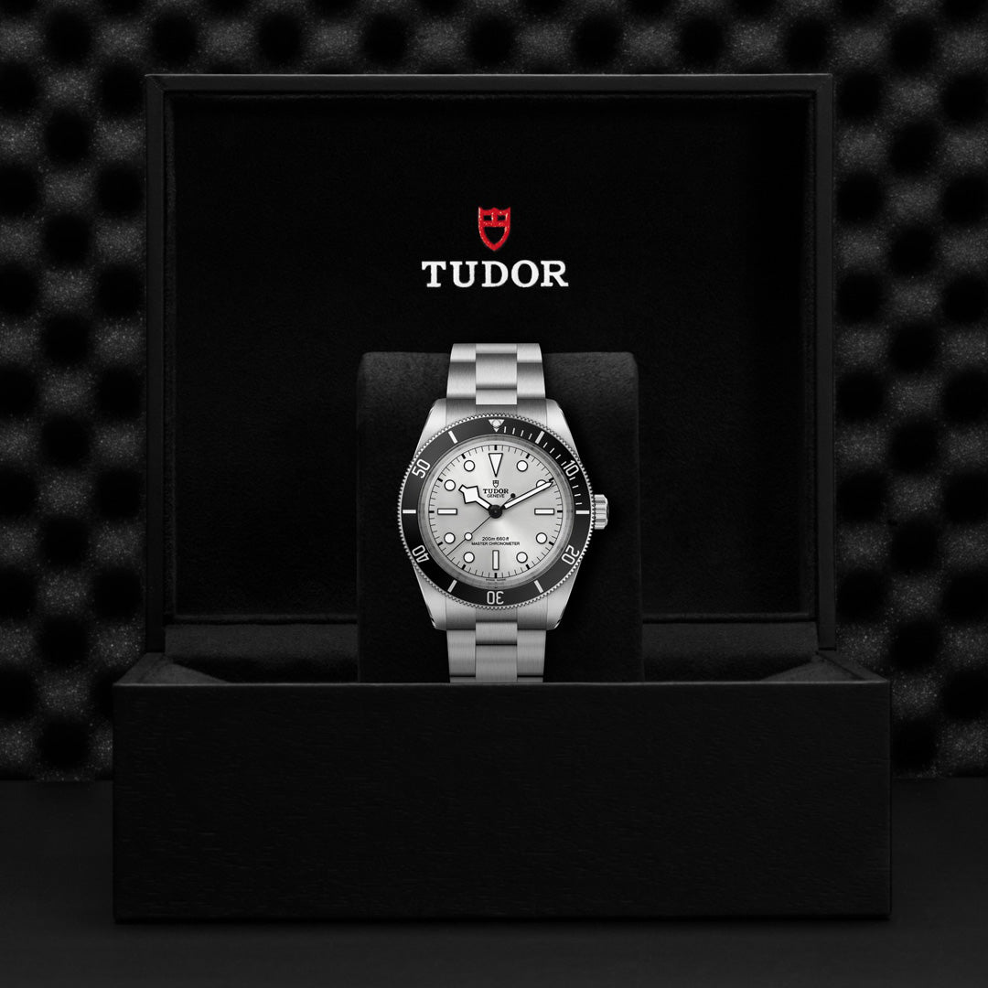 The TUDOR Black Bay 68 wristwatch is displayed in an open black box with a metallic strap. Its round dial features luminous markers, a bezel, and the TUDOR name with the red logo, showcasing the precision typical of this masterpiece.