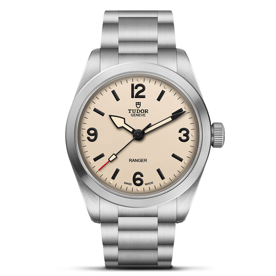 The TUDOR Ranger by TUDOR is a stainless steel wristwatch with a cream dial, black hour markers, numerals at 12/3/6/9 o’clock, simple black hands with a red-tipped seconds hand, and a metal bracelet.