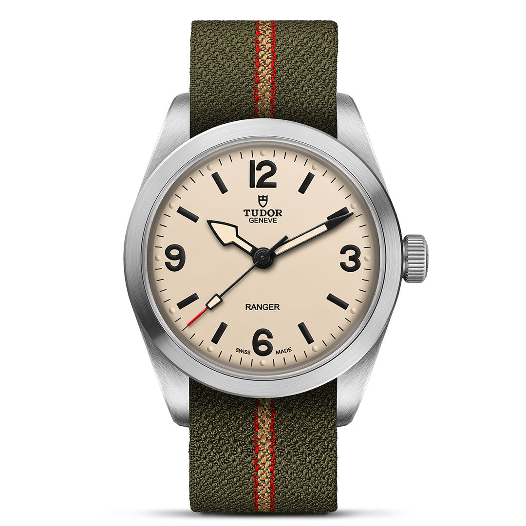 The TUDOR Ranger by TUDOR features a beige dial with bold black numerals and markers, a silver bezel, and an olive green fabric strap with a red stripe. Inspired by expedition watches, it offers excellent legibility.